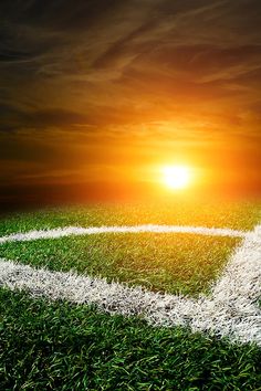 a soccer field with the sun setting in the background and grass on the sidelines