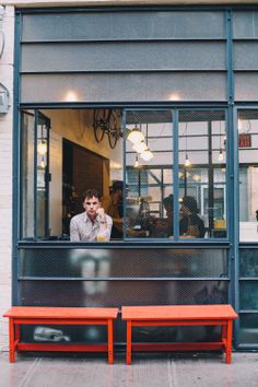 a man sitting at a table in front of a window with an orange bench next to him