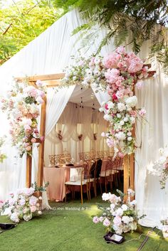 an outdoor ceremony with white drapes and pink flowers on the arch over the tables