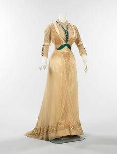 Haute couture fashion dress gown from American 1909-1911 Edwardian Style. Made in silk with lace,  trim, and metal bead. Green emerald contrasting fabric and laces on the decollete, bodice and sleeves with drape and decorated skirt at the front and tassel frill and train at the back. Mrs. Dunstan is a well known New York dressmaker. Her work of high style dress exhibits the typical techniques used in that period, such as the bolero and vestee configuration of bodice and over the shoulder panels. 1890s Dress, 1900s Dress, Dress And Shoes, Tea Gown, 1900s Fashion, 1910s Fashion, Edwardian Dress, Costume Collection, Vintage Gowns