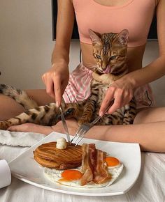 a woman is sitting on the bed with her cat while she cuts up some food