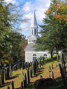 a church with a steeple surrounded by trees and headstones in front of it