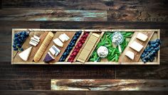 a wooden tray filled with assorted cheeses and grapes on top of a wood floor