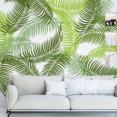 a white couch sitting in front of a wall with green leaves on it