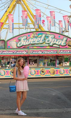 a girl standing in front of a carnival ride holding a pink heart shaped pillow with the word sweet spot on it