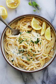 a bowl full of pasta with lemon and parsley on the side, ready to be eaten