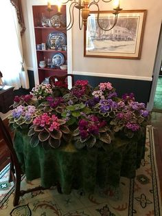 a dining room table with flowers on it in front of a painting and chandelier