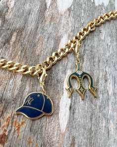 a gold chain with a blue baseball hat and two charms on it, sitting on top of a piece of wood