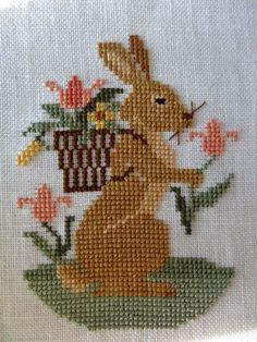 a cross stitch bunny holding a basket with flowers