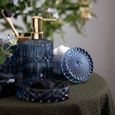 an assortment of blue glass items on a table with flowers in the backgroud