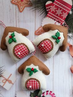 three felt christmas ornaments on a white wooden table with pine branches and decorations in the background