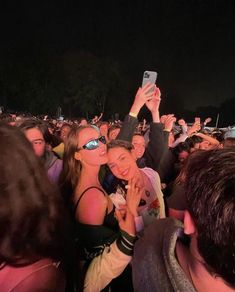 a group of people taking pictures with their cell phones at an outdoor music festival in the evening