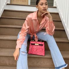 a woman is sitting on the steps with her hand in her pocket and holding a pink purse