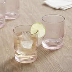 three glasses on a table with a lime slice in the middle and another glass next to them