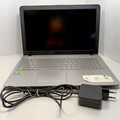 an open laptop computer sitting on top of a white table next to a charger