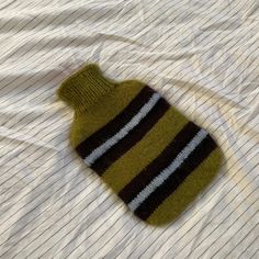 a green and black striped sweater laying on top of a white bed sheet next to a pillow