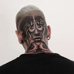 the back of a man's head with tattoos on his face and behind him