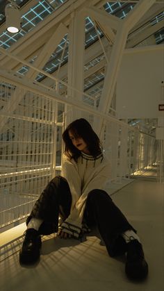 a woman sitting on the ground in front of a white wall and metal railings