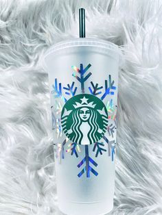 the starbucks cup has snowflakes on it and is sitting on a fluffy white surface