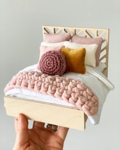 a person holding up a crocheted bed with pink and white pillows on it