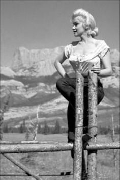 a woman leaning on a fence with mountains in the background