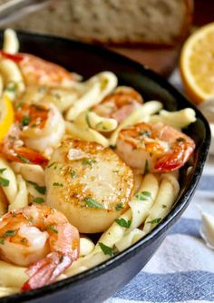 a pan filled with pasta and shrimp on top of a table next to lemon wedges