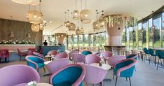 the interior of a restaurant with pink and blue chairs, chandeliers and tables