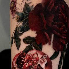 a woman's arm with flowers and pomegranates on it