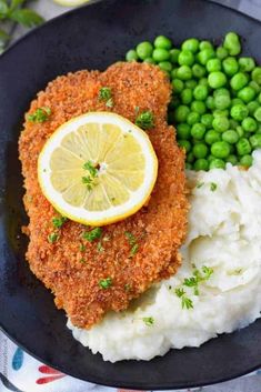 chicken with mashed potatoes, peas and lemon wedges on a black platter