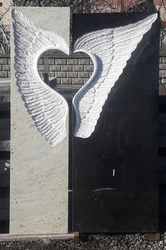 a large white angel wing is on the side of a black and gray wall next to a brick building