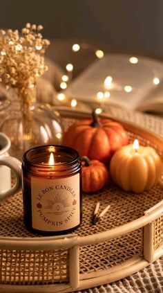 a candle sitting on top of a wicker tray next to coffee cups and pumpkins