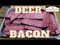 a metal tray filled with bacon sitting on top of a wooden table next to a sign that reads deer bacon