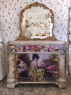 a dresser with a painting on it in front of a mirror and wallpapered walls