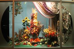 a window display with flowers and plants in the front, behind which is a curtain