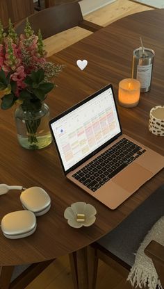 an open laptop computer sitting on top of a wooden table next to flowers and headphones