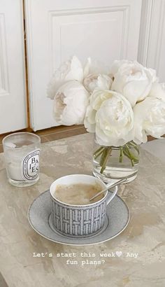 there is a cup and saucer on the table with flowers in front of it