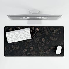 a computer mouse and keyboard on top of a black desk mat with skulls and leaves