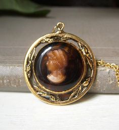 Vintage brown glass lady cameo pendant necklace. This unsigned necklace is circa-1960's.  Goldtone metal with brown glass background.  Cameo is glass, I think. Chain measures 16" and closes with a spring-lock clasp. Wonderful Victorian look to this.  In great shape! Sorry, but no international shipping at this time. Please see my shop for more vintage, estate jewelry: nightowlmemories.etsy.com Vintage Antique Gold Cabochon Jewelry, Vintage Brass Necklaces With Cabochon, Formal Bronze Cameo Jewelry, Vintage Brown Necklace For Gifts, Vintage Brown Necklace For Gift, Vintage Bronze Cameo Necklace, Collectible Cameo Costume Jewelry Necklaces, Vintage Intaglio Pendant Jewelry, Formal Cameo Brass Necklace