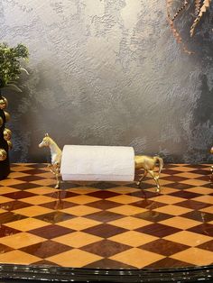 two golden horses are standing on a checkered table top with a roll of toilet paper