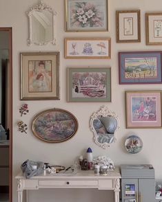 there are many framed pictures on the wall next to a white table with a drawer