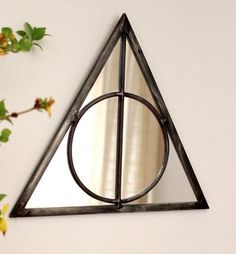 a triangle shaped mirror mounted to the side of a white wall next to a plant