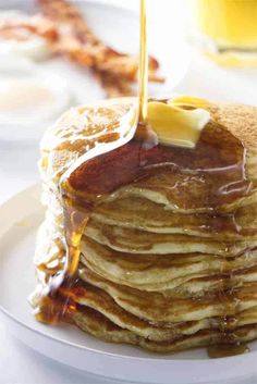 a stack of pancakes with syrup being poured onto them and topped with butter on the side