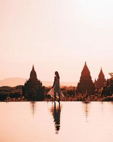 a woman is standing on the edge of a pool in front of some pagodas