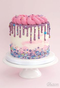 a white cake with pink frosting and sprinkles on it sitting on a plate