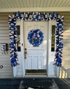 a blue and silver wreath on the front door of a house with decorations around it