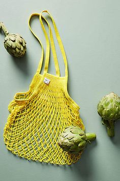 two artichokes and a mesh bag on a gray surface, one with a yellow handle