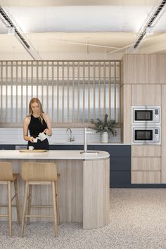 a woman is standing in the middle of a kitchen with an island and stools