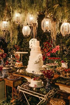 a table topped with a white cake covered in lots of greenery and hanging lights