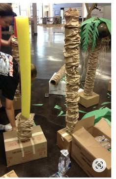 two people are making palm trees out of cardboard boxes and other items in the background