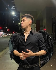 a man in black shirt standing on sidewalk next to street with large bird wings around his neck